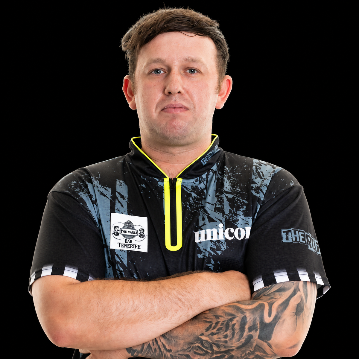 Darts player Callan Rydz in his sponsored match shirt, arms crossed, tattooed sleeve on display