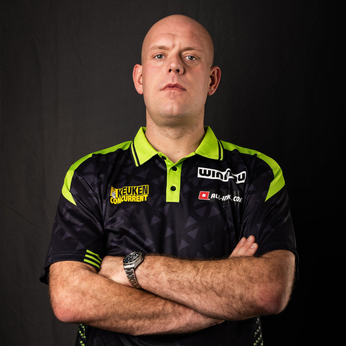 Darts player Michael van Gerwen in his sponsored player shirt, arms crossed, dark studio background