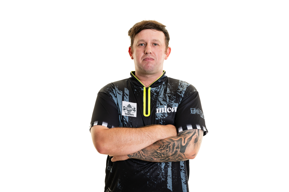 Darts player Callan Rydz in his sponsored match shirt, arms crossed, tattooed sleeve on display