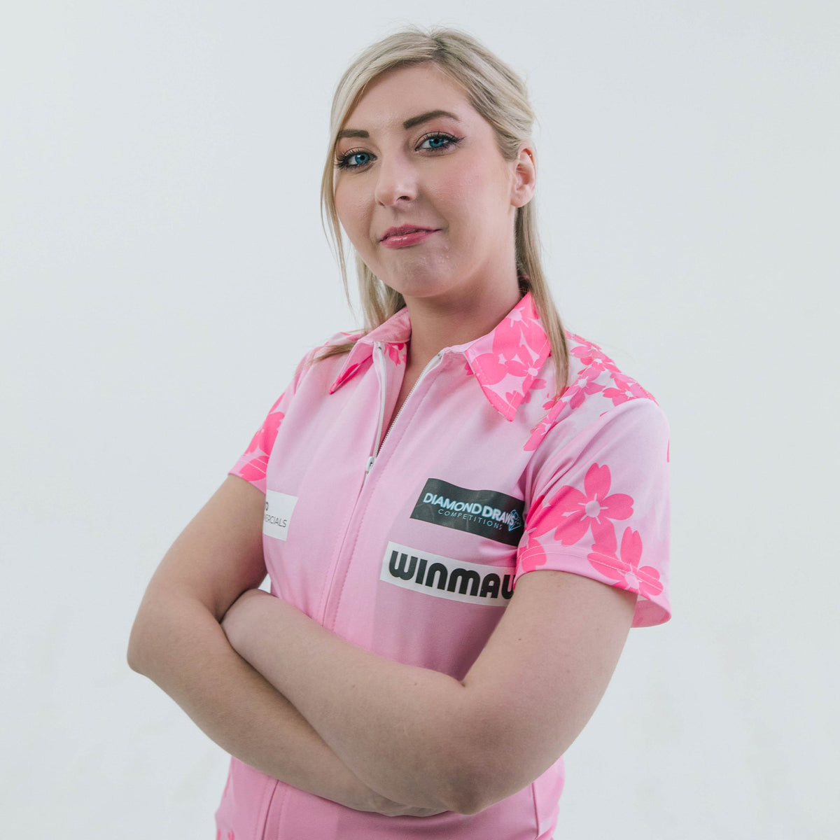 Darts player Fallon Sherrock in her pink Winmau player shirt, arms crossed, plain white studio background