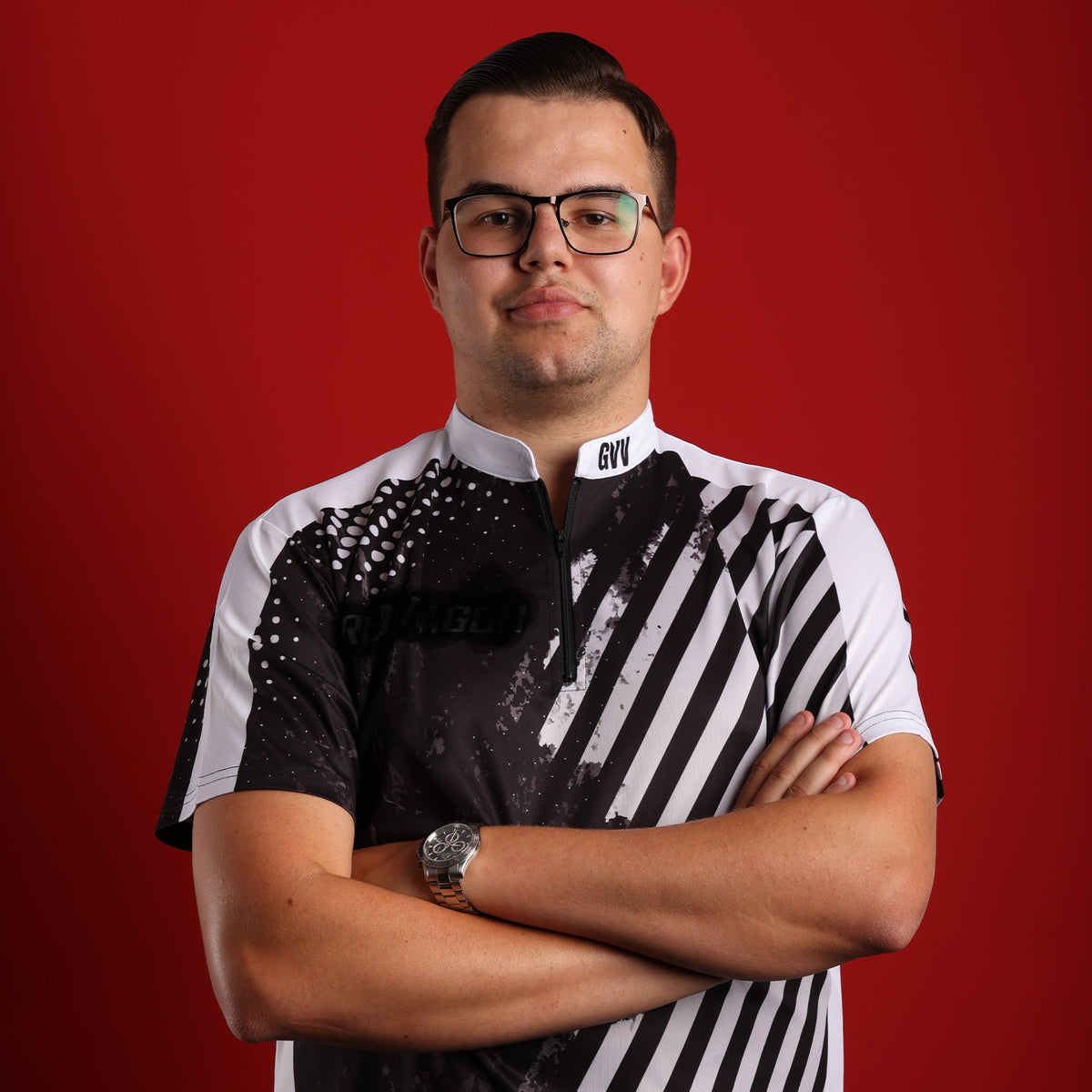 Darts player Gian van Veen in glasses and his GVV player shirt, arms crossed, red studio background